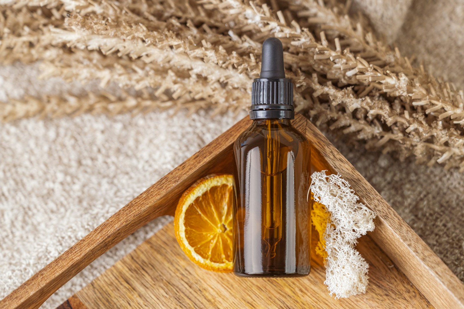 eine braune Glasflasche mit Pipette neben einer Orangenscheibe auf einem Holztablett