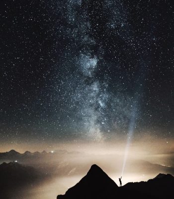 Silhouette einer Person die Sternzeichen begeistert ist und auf dem Gipfel des Berges, bei Nacht mit einer Taschenlampe auf einen mit Sternen gefüllten Himmel zeigt
